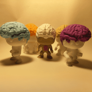 El simpático muñeco Brainvis sentado, sonriendo, con sus característicos lóbulos cerebrales de colores formando su cabello, junto al logotipo de la marca YOAM.