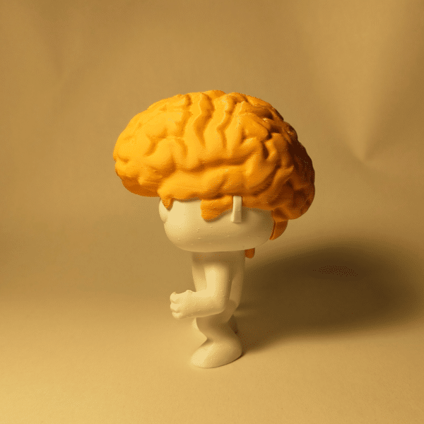 El muñeco Brainvis colocado elegantemente en el escritorio de un neurólogo o psicólogo, junto a una computadora y una planta pequeña.