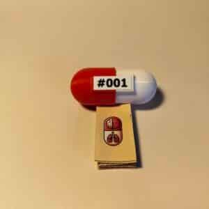 Píldora Anatómica sorpresa: Llavero con mini modelo anatómico de cerebro. Cápsula roja etiquetada como #001 abierta, revelando una pequeña maqueta cerebro blanca en su interior junto a un kit de llavero.