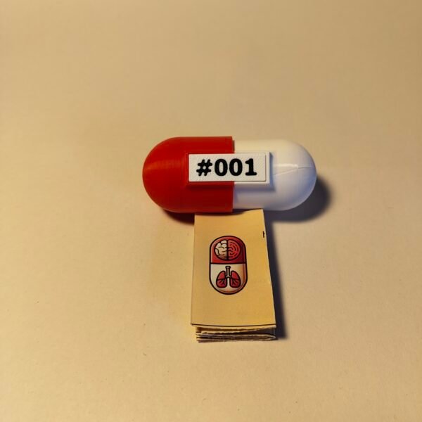 Cápsula roja etiquetada como #001 abierta, revelando una pequeña maqueta cerebro blanca en su interior junto a un kit de llavero.